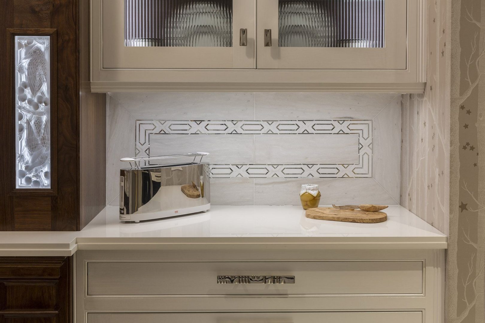 AKDO's White Haze marble and Allure radiance silver mirror border create sophisticated backsplash alongside warm wood cabinetry by Clive Christian and genuine Lalique crystal backlit inset panels.